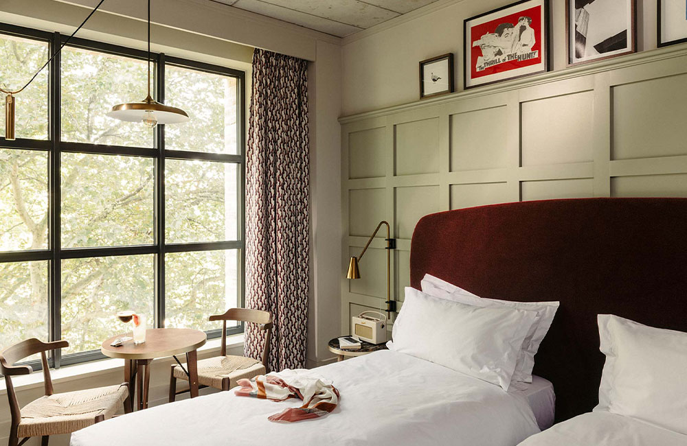 Showcasing the room with a large window allowing natural light to illuminate the twin beds