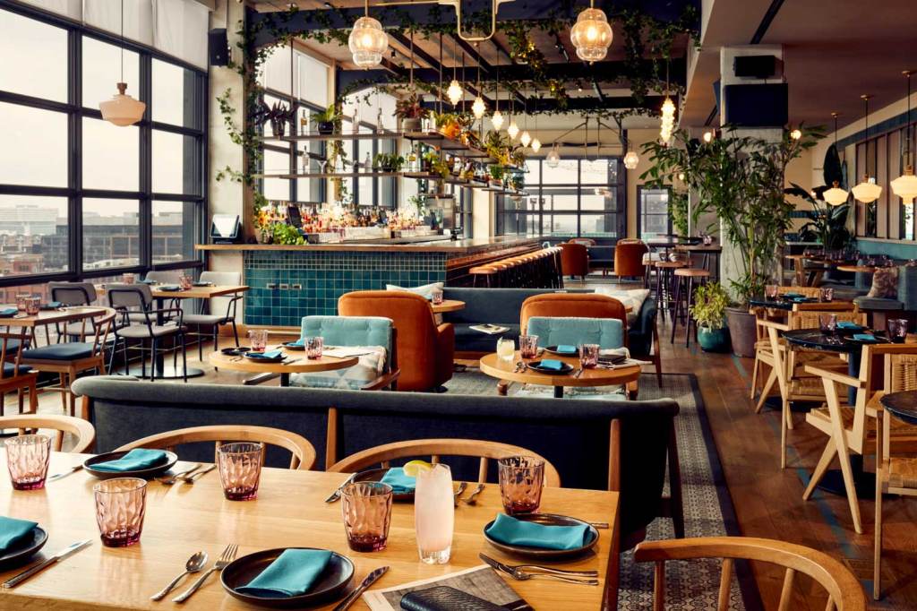 The restaurant has a variety of different sized tables, floor to ceiling windows and lots of plants