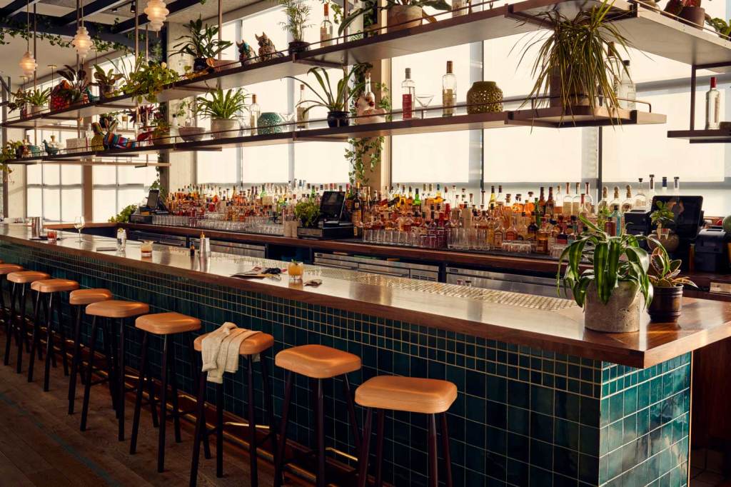 The bar has a row of bar stools in front of it, and many, many bottles of alcohol behind it