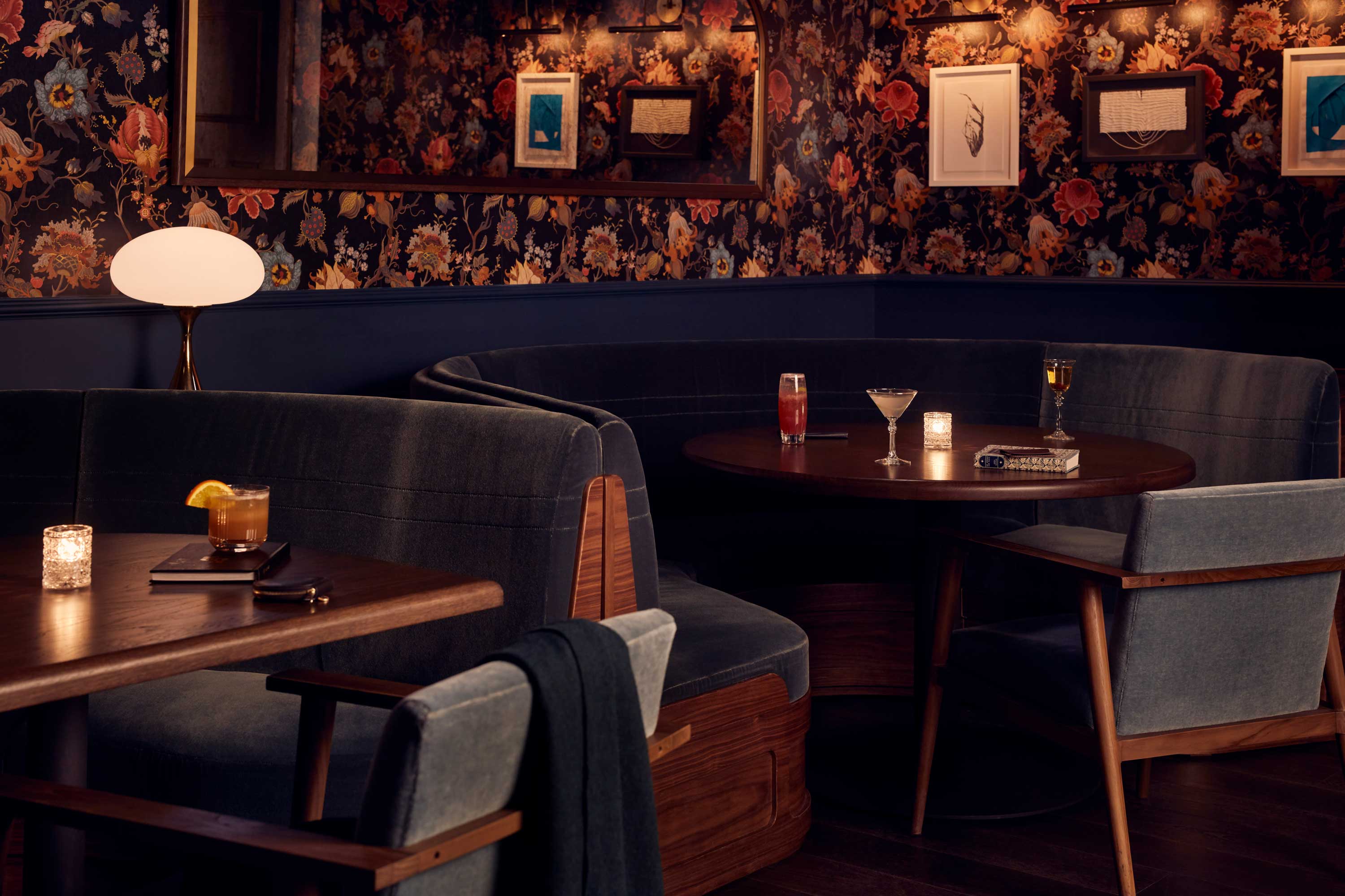 Cocktails sit on tables in the middle of comfortable seating booths in a dimly lit, intimate setting