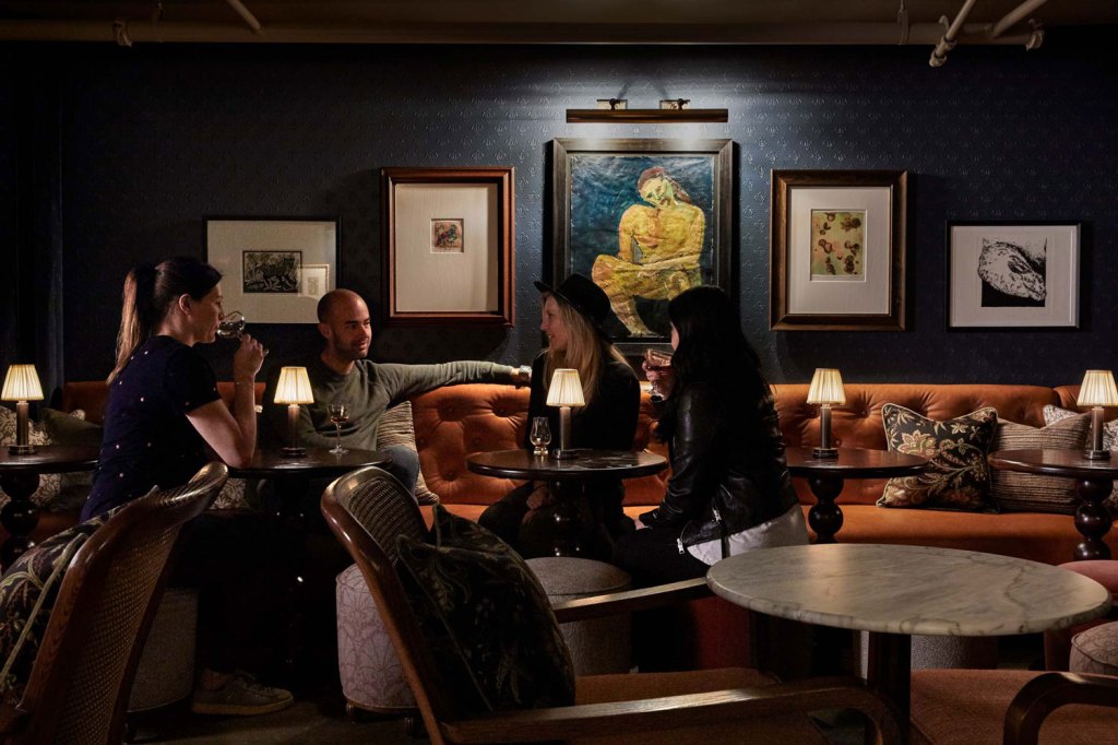 Four people hang out in the basement bar in Portland, which is dimly lit and decorated with modern art on the walls