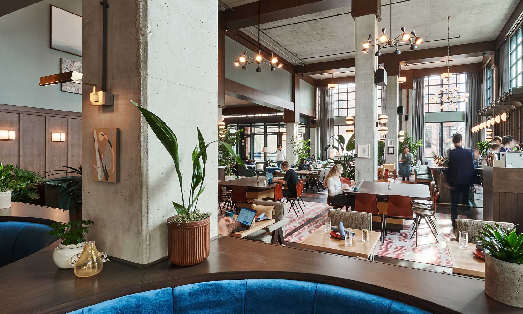 A few guests sit in the restaurant and lobby of the hotel, which has high ceilings and industrial decor