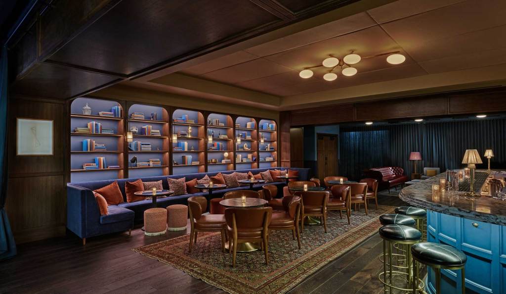 The back wall of the bar has shelving with different books and vases, with a variety of different seating in front of it