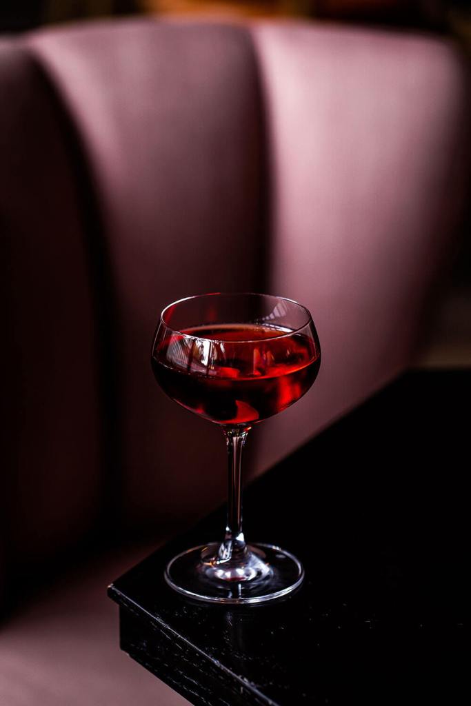 A red cocktail served in a coupe glass