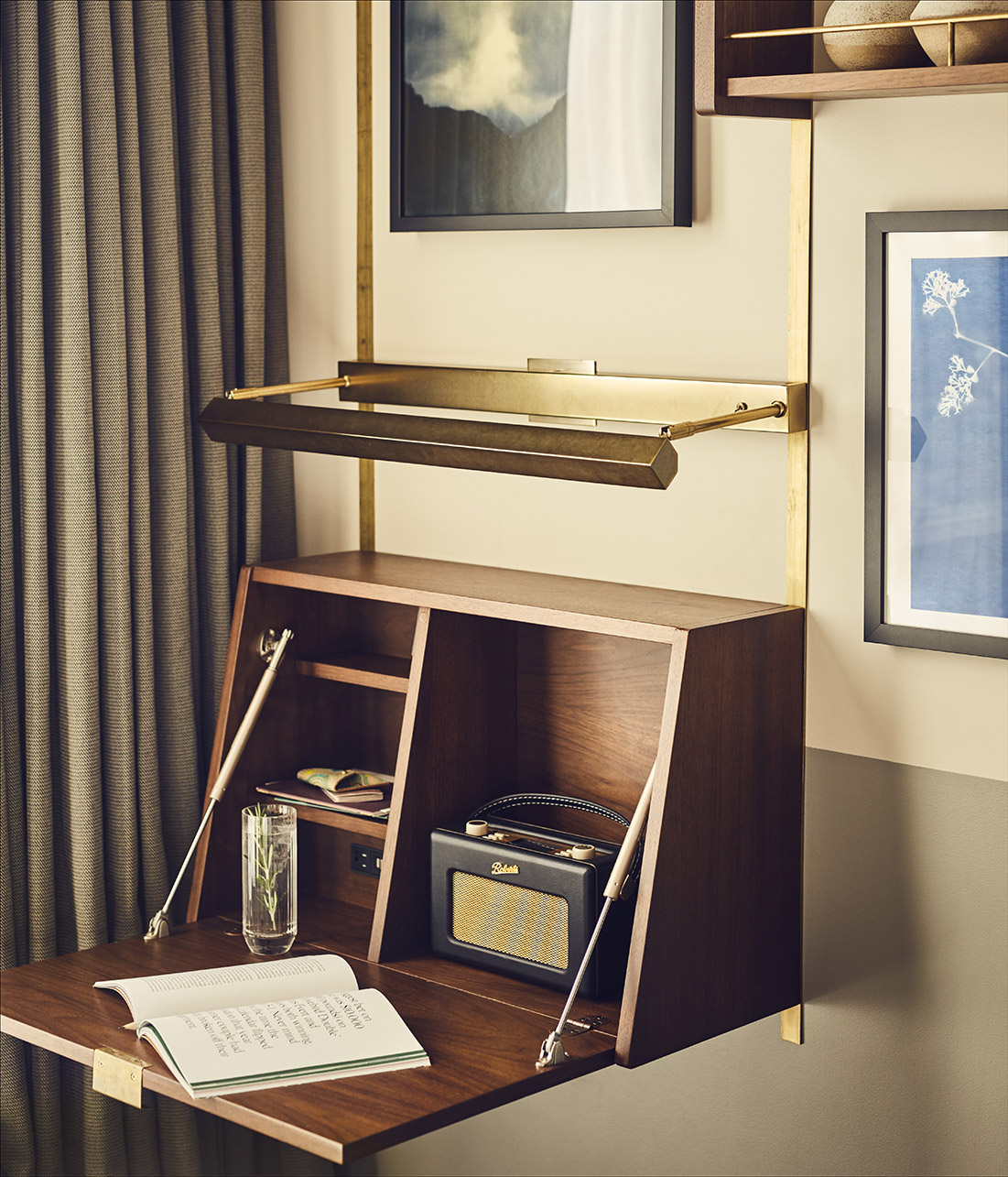 Artwork, radio and shelving all on the wall opposite the bed in the hotel room.
