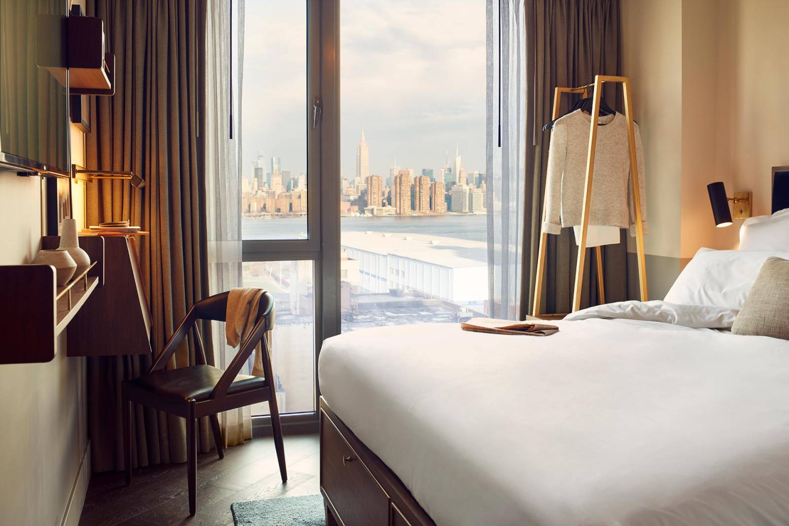 Room interior with views of Manhattan, a desk and large bed.