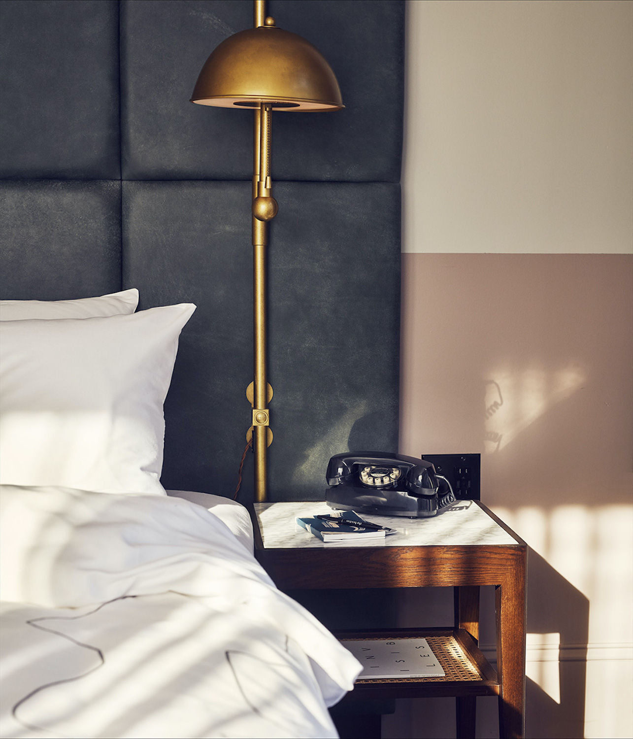 A gold lamp sits above a bedside table which has an old-fashioned black telephone