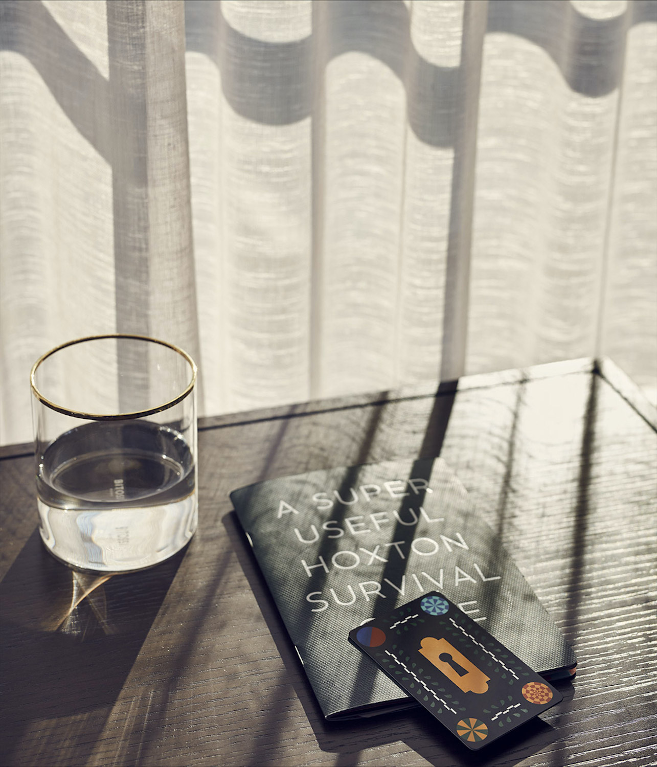 Glass of water, room key and our Hoxton "survival guide" sat on a table