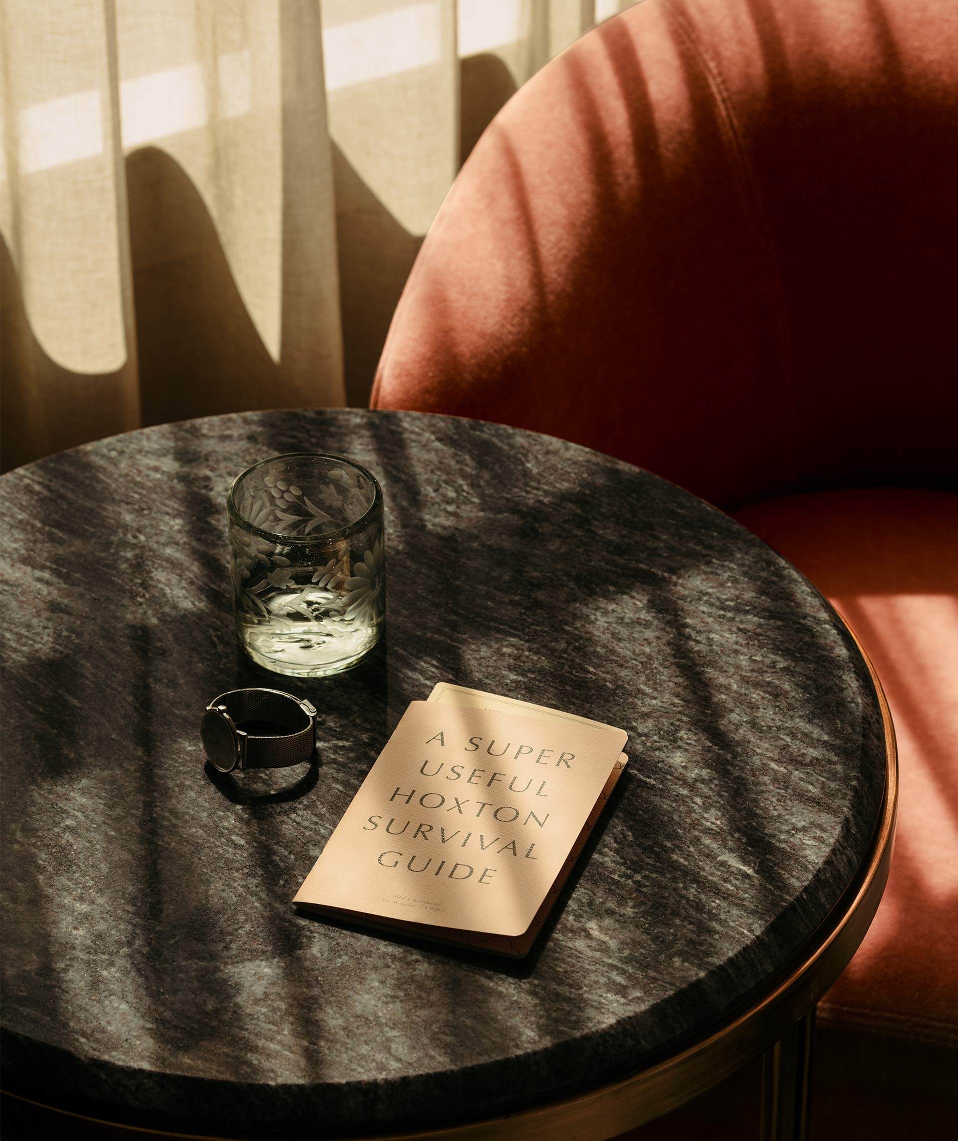 Glass of water, a watch and our Hoxton "Survival Guide" on a table beside a lounge chair