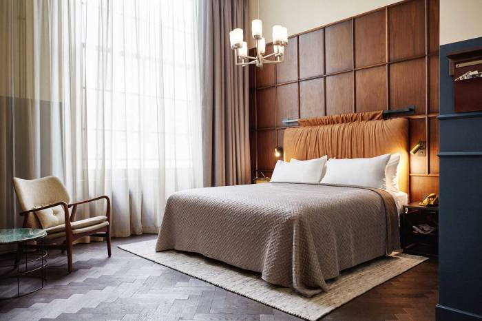 Wide view of a grand room with double bed and dark wood floor and wall panelling with chandelier visible.