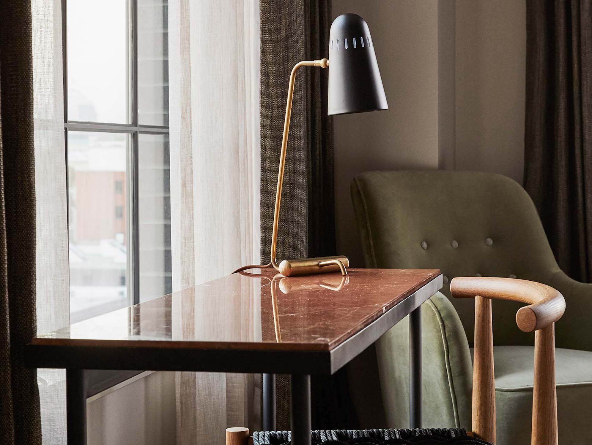 A black table lamp sits on a small desk in front of the window