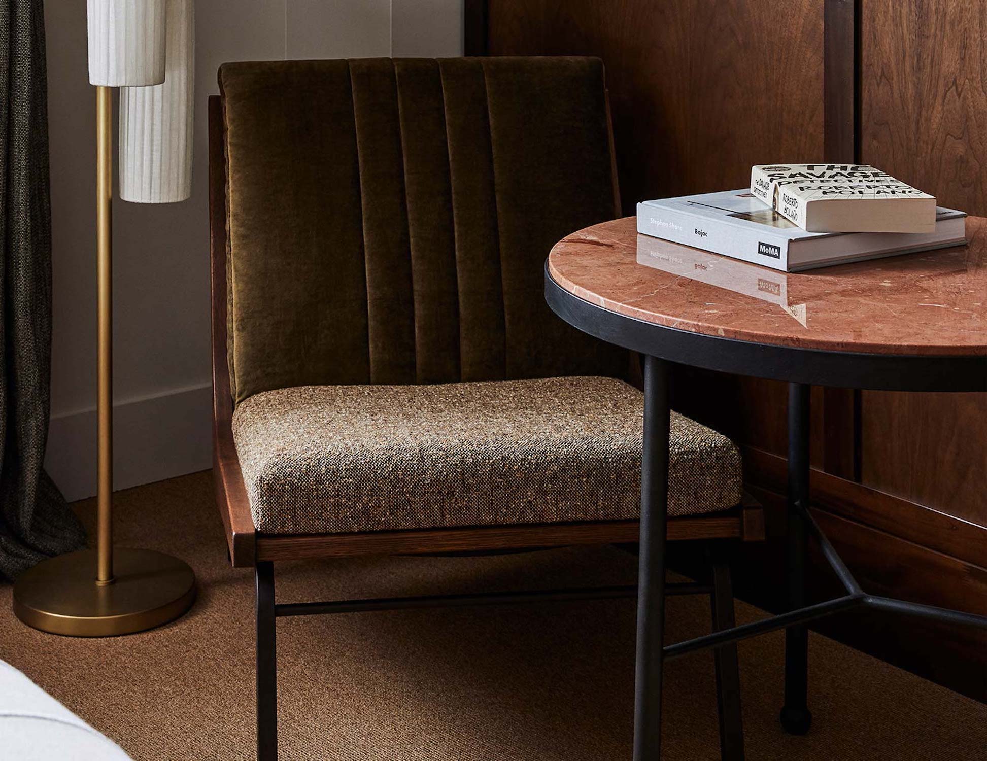 Two books sit on a table beside a dark olive green lounge chair and floor lamp