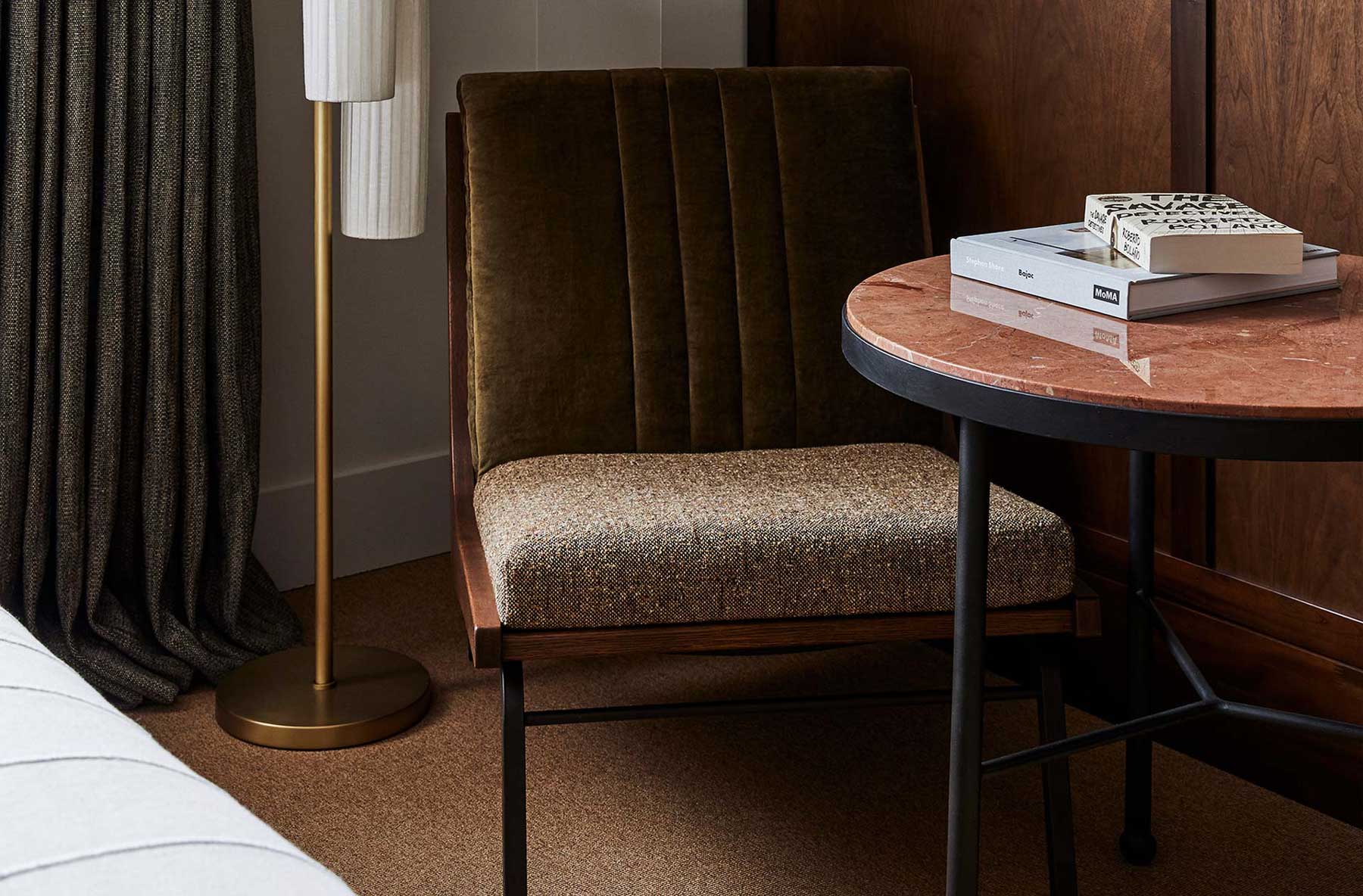 Two books sit on a table beside a dark olive green lounge chair and floor lamp