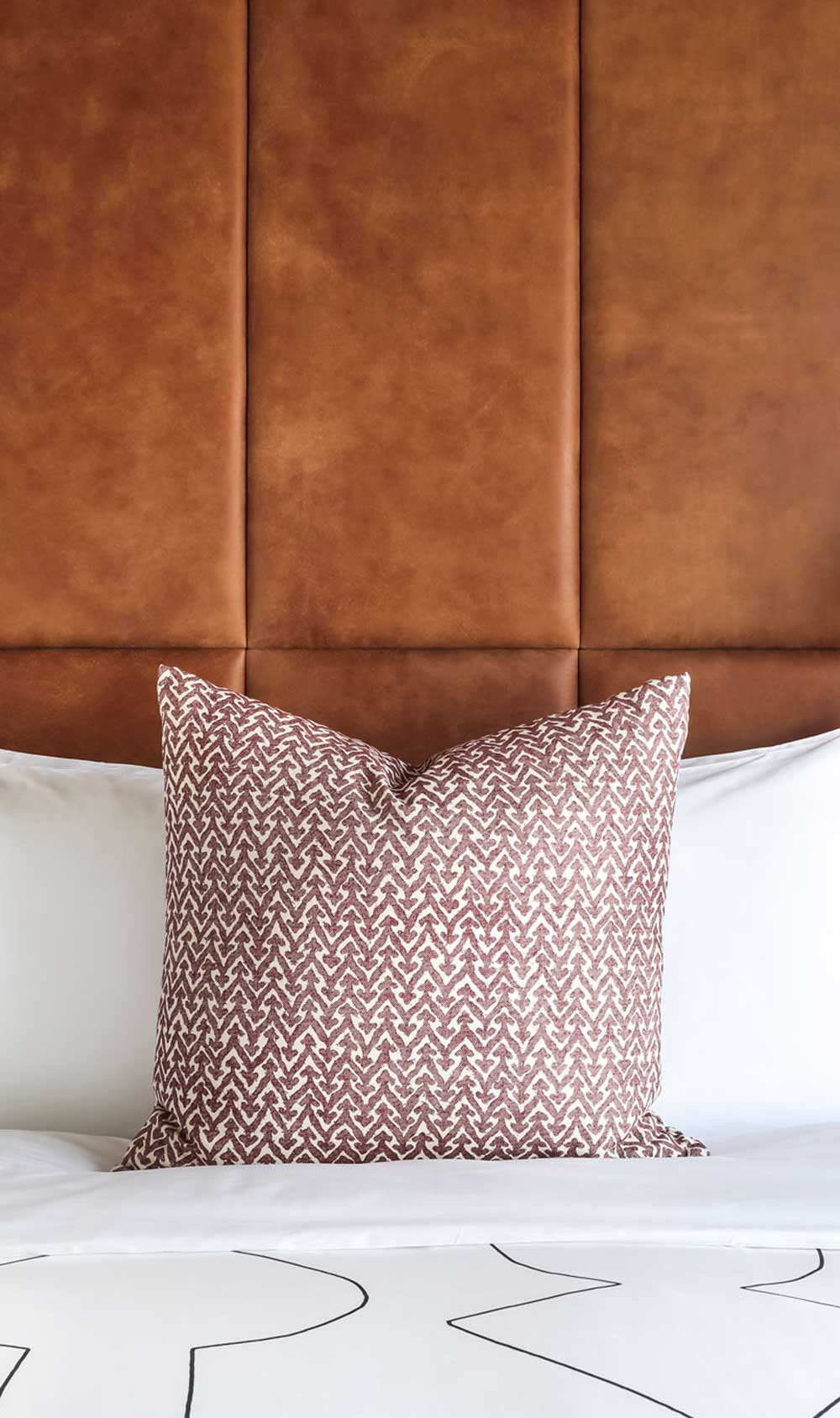 A dusky pink cushion sits in front of crisp white pillows on the bed