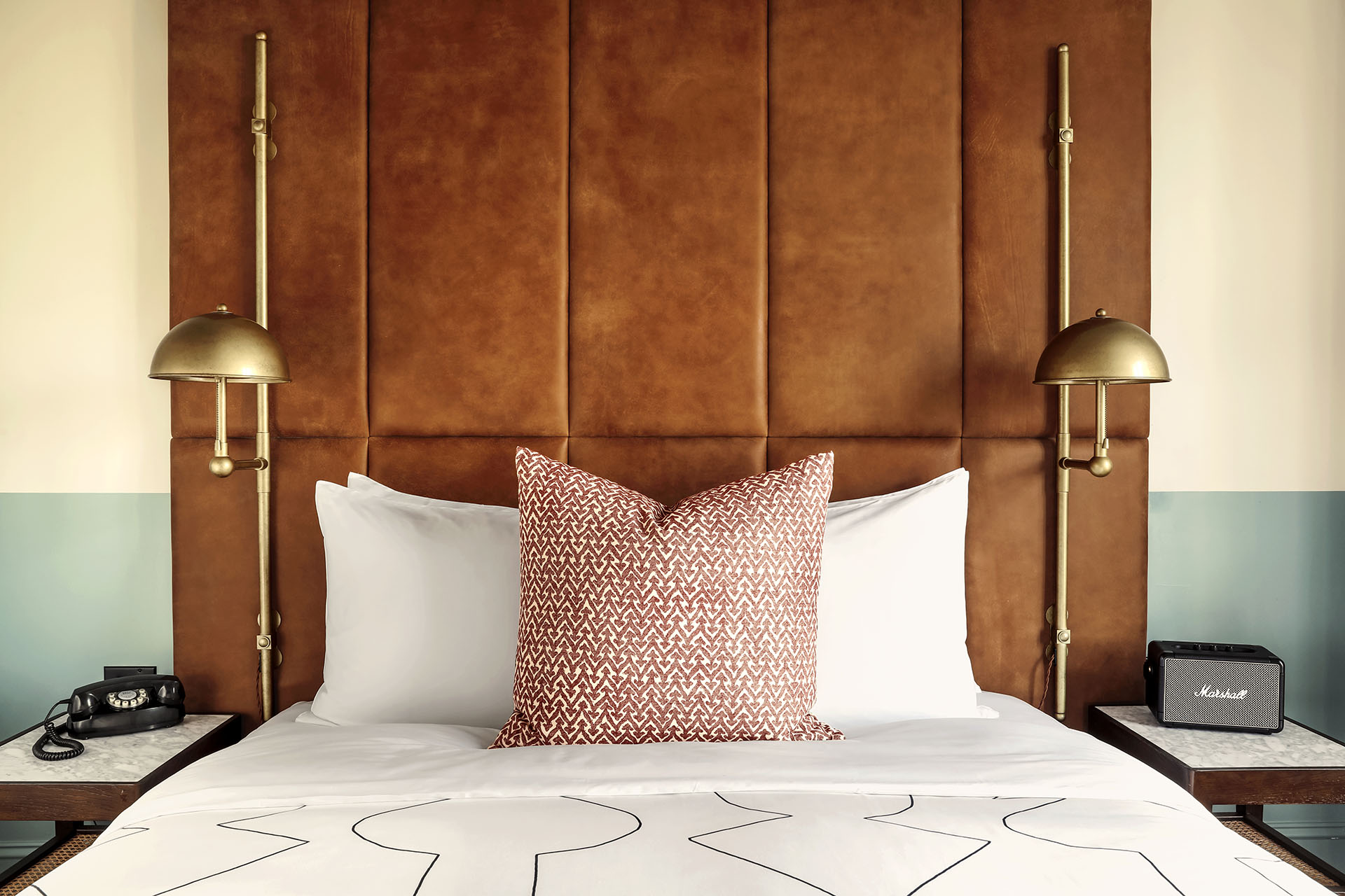 Queen sized bed with white bed linen, a patterned cushion and caramel coloured leather headboard