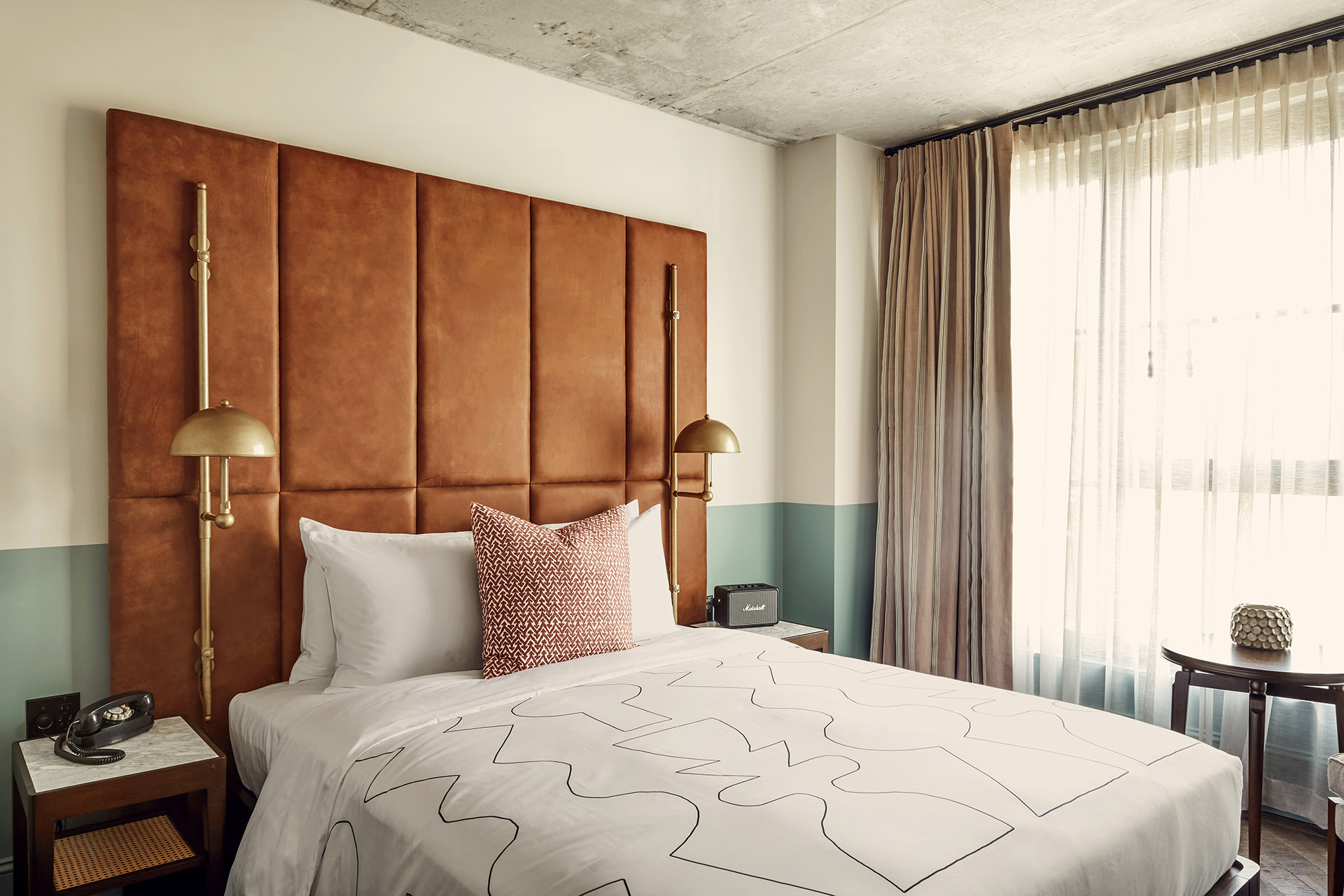 Queen sized bed in a guest room with a Marshall radio on one side, and a telephone on the other