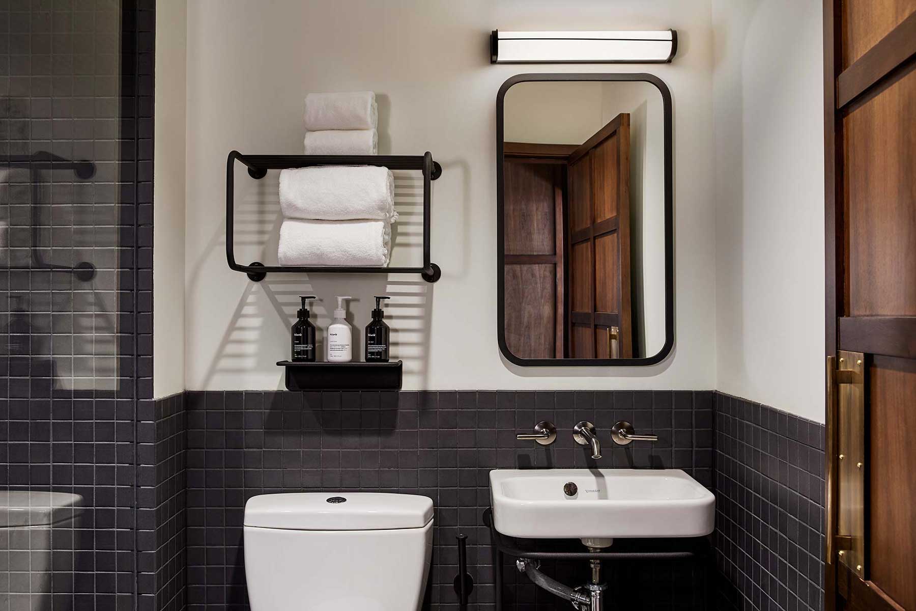White towels and bathroom products sit on shelves above the toilet on the left, whilst a mirror and light sit above the sink on the right