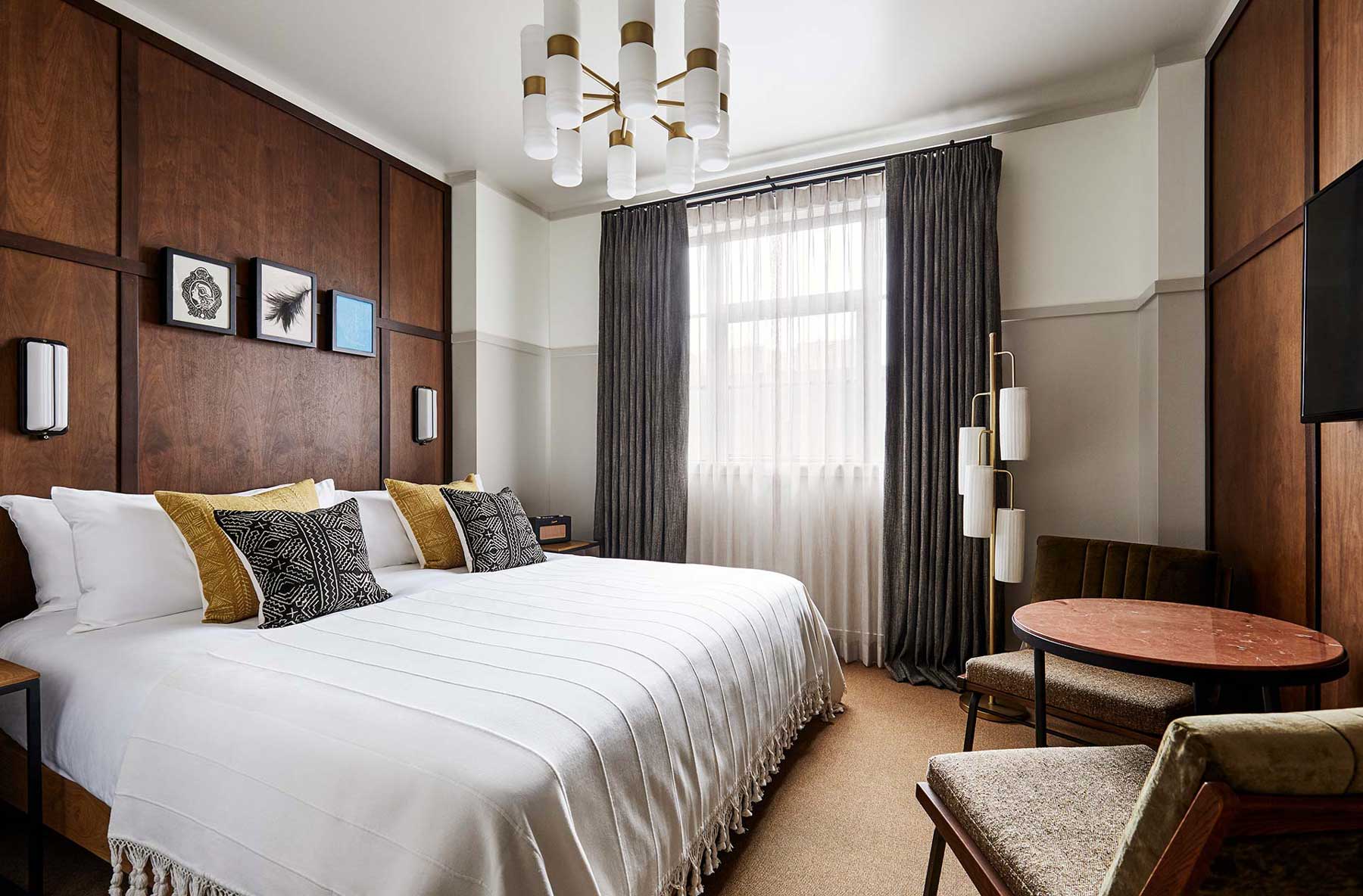 The walls both behind and opposite the bed consist of dark wooden panels, whereas the adjacent wall around the window is painted white and light grey