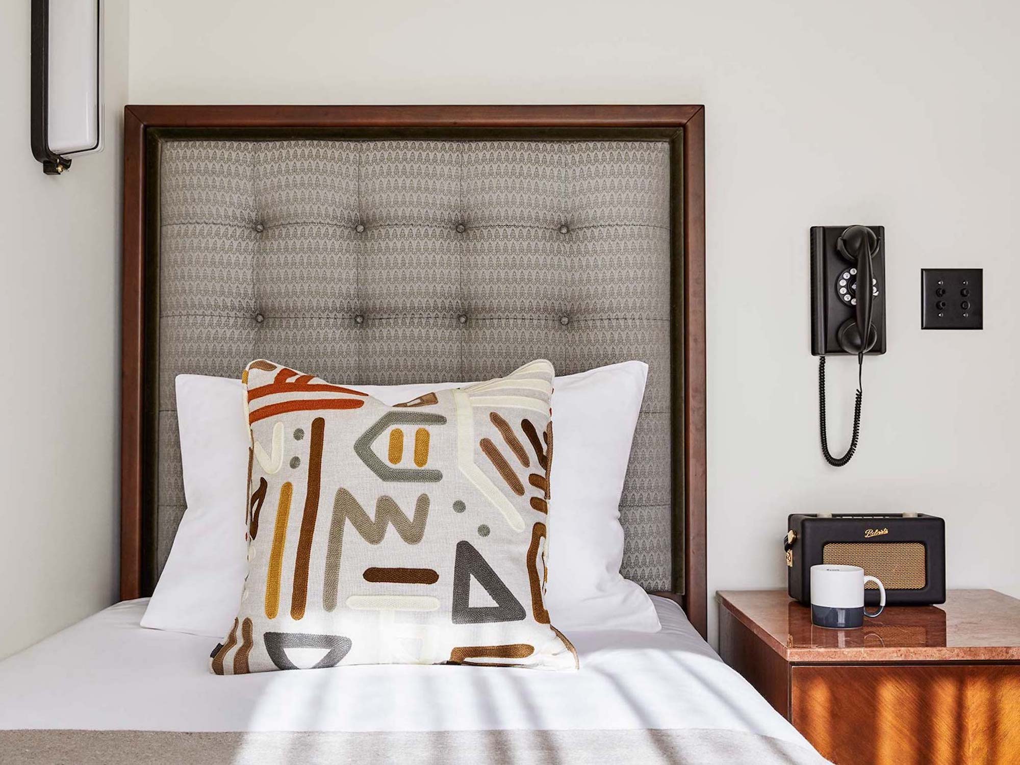 A large patterned cushion sits on a single bed in a Snug Room, with the telephone hanging on the wall beside it