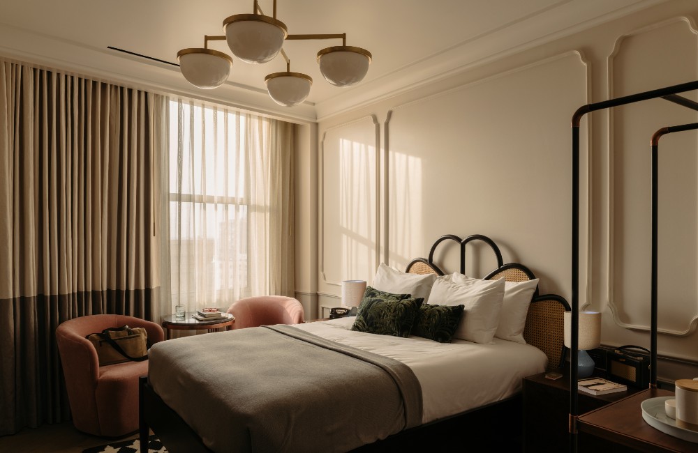 Cozy King room featuring a spacious king-size bed, two soft pink velvet chairs next to a large window, and a table.