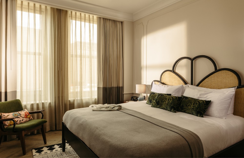 Cozy King room featuring a spacious king-size bed, one green velvet armchairs next to a large window letting abundant natural light into the room.