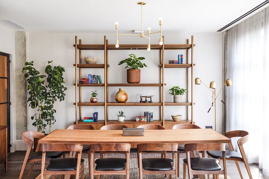 Decorative shelving sits on the far side of the meeting room, with a long table and 10 chairs around it in the middle. There is a full length window on the right hand side with lots of natural light.