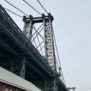 Looking up at the Williamsburg Bridge from the ground, on a grey-blue sky day