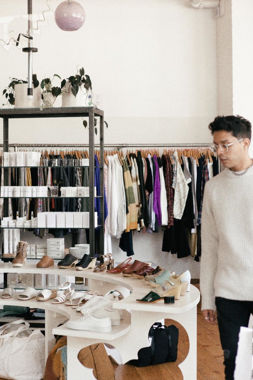A man looks at shoes on display in front of shelves and a long rail of clothing
