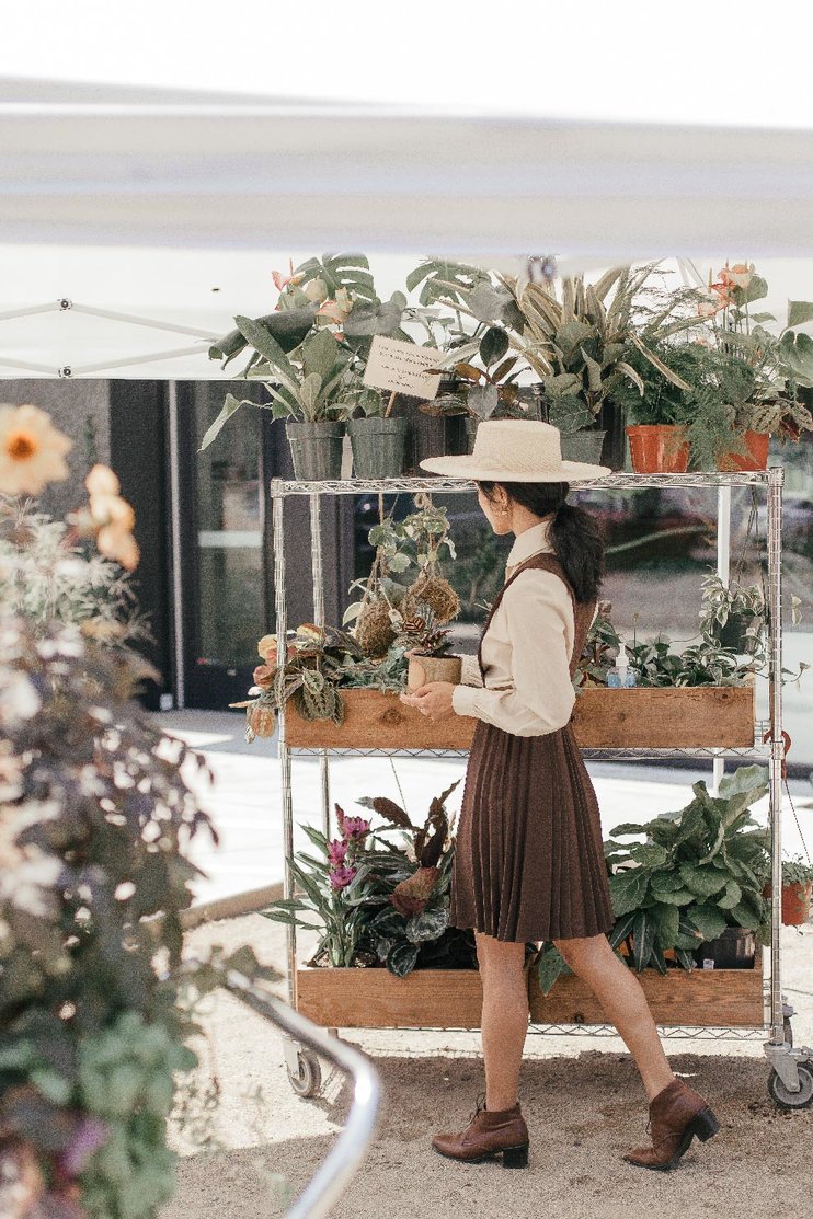 A woman with long dark hair tends to plants on display under a white canopy