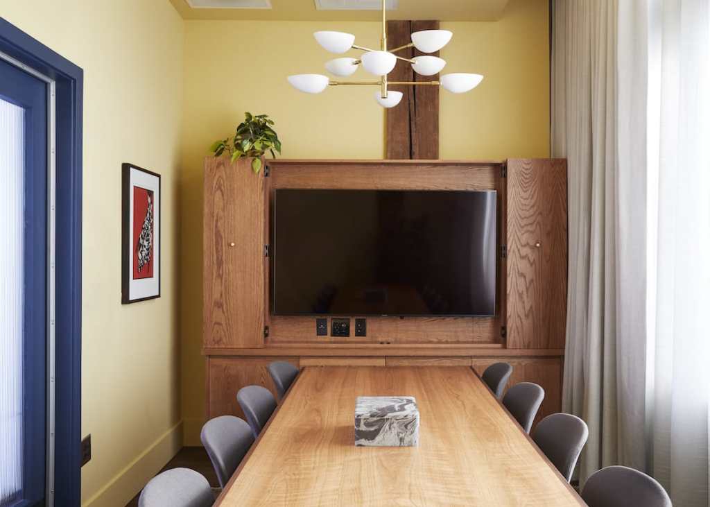 A small meeting room, with a long table for up to ten people, in front of a TV