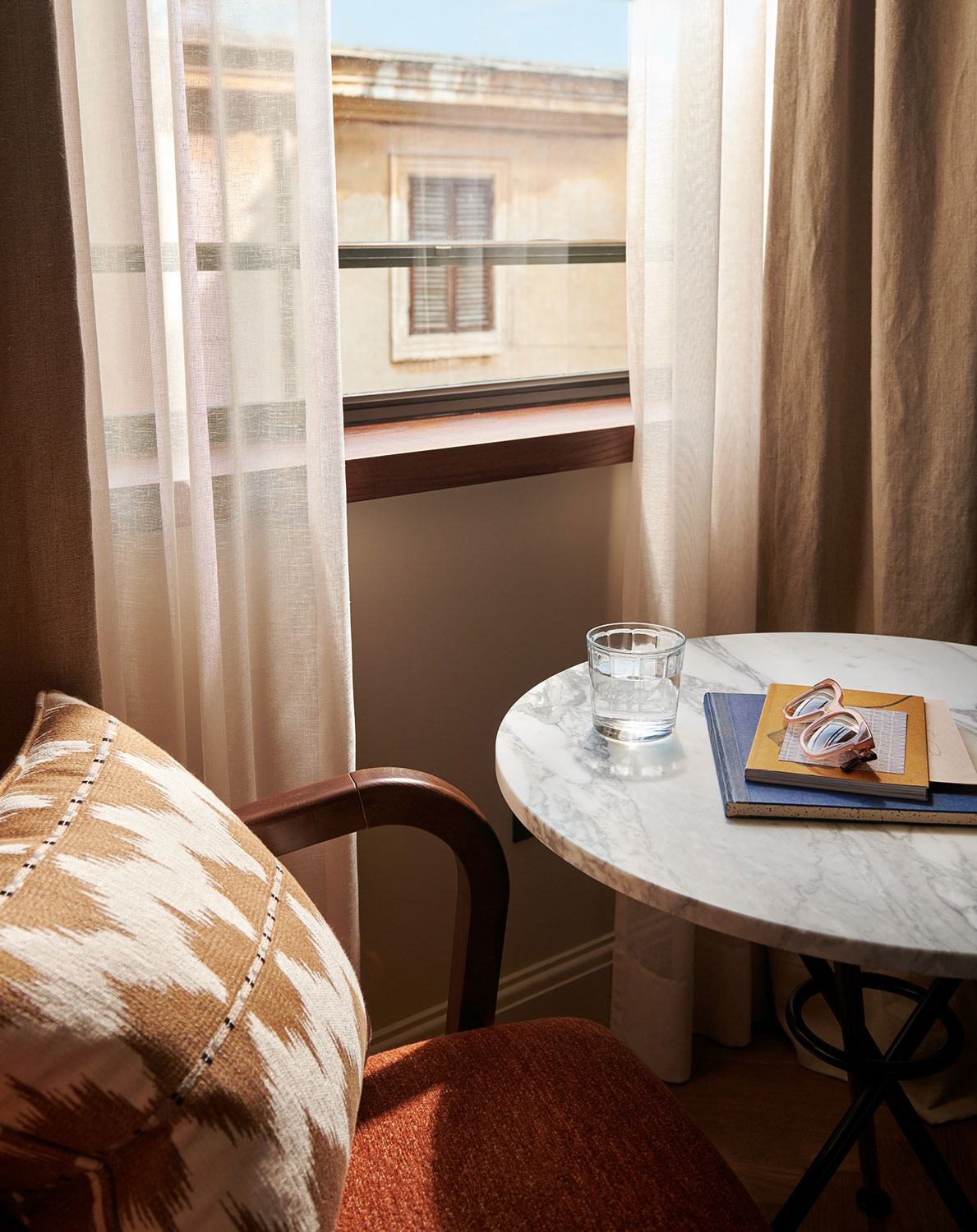 A glass of water sits on a marble table beside a lounge chair in the hotel room