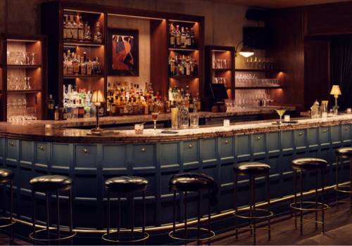 Dimly lit bar area, with several black bar stools in front of it
