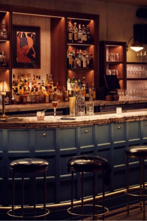 Dimly lit bar area, with several black bar stools in front of it