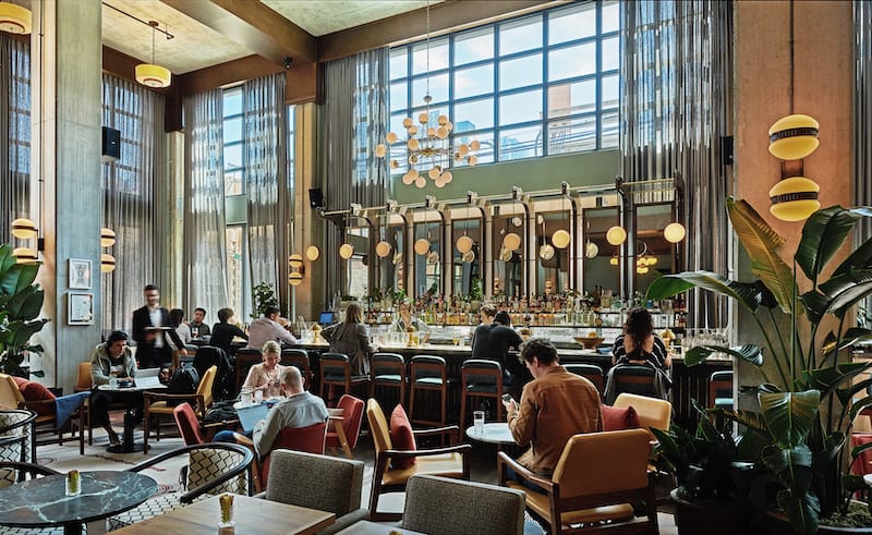 People seated in lobby area beside the bar, which has very high ceilings