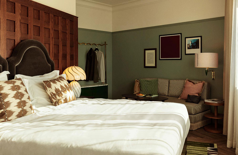 Sunlight streams onto a large double bed, with a sofa and clothes area in the background