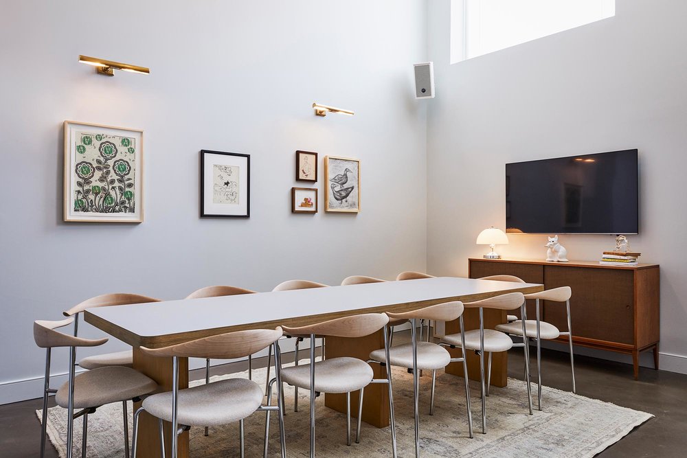 The Library meeting room in Williamsburg has a long table with 10 chairs and a TV on the wall