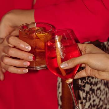 A cocktail and wine glass clink in two women's hands