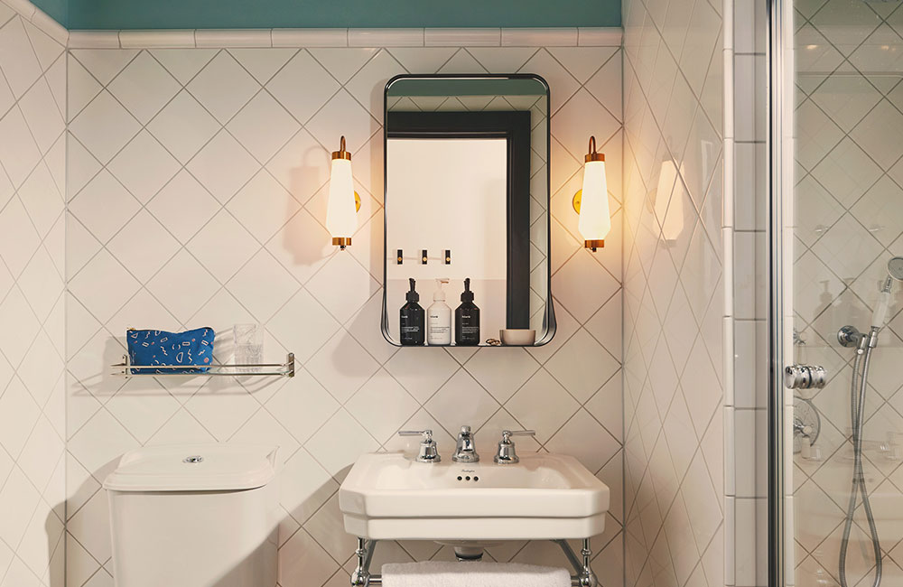 A very bright ensuite bathroom with toilet, sink and shower. Bathroom products sit on a shelf on the mirror above the sink.