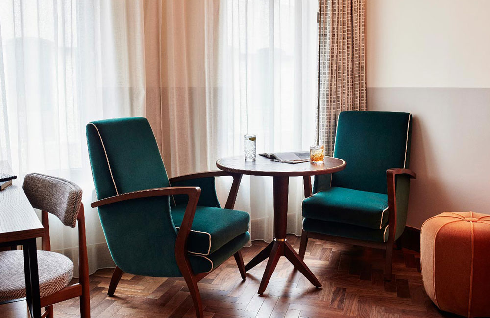 Two velvet lounge chairs and a table in front of full length windows