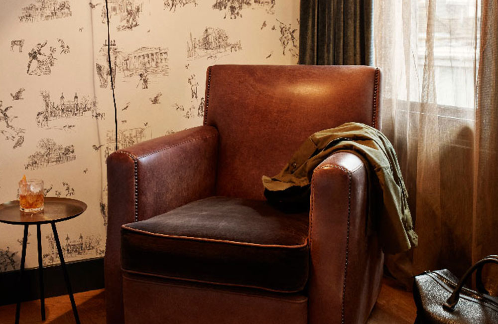 A leather chair sits in the corner of the room, will illustrative wallpaper behind