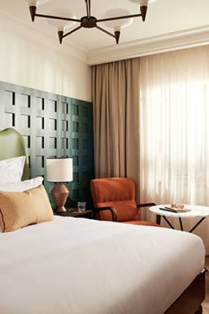 Large bed in front of green wood-panelled wall with two orange lounge chairs