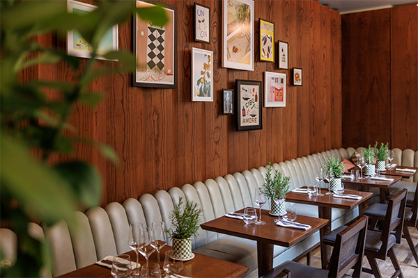 Long wall-mounted sofa with tables and chairs in with several art pieces hanging on the wall above.
