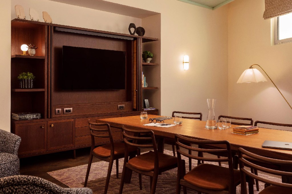 Meeting room with long table and 8 visible chairs, with large TV screen at the end of the table. Water, books, pencils and a laptop are on the table.