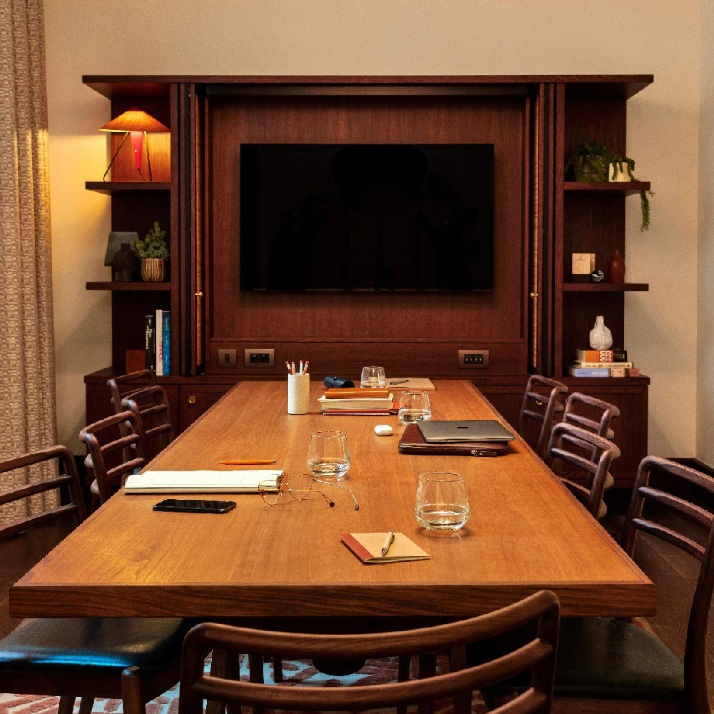 Meeting room with table and seating for 8 people, and a large TV screen at the opposite end
