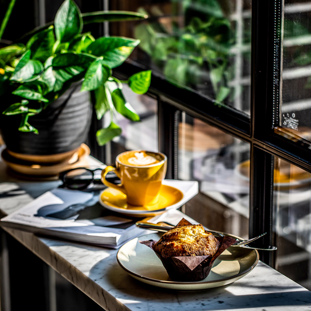 Tasse Kaffee und ein Muffin auf einem Tisch neben einer Pflanze