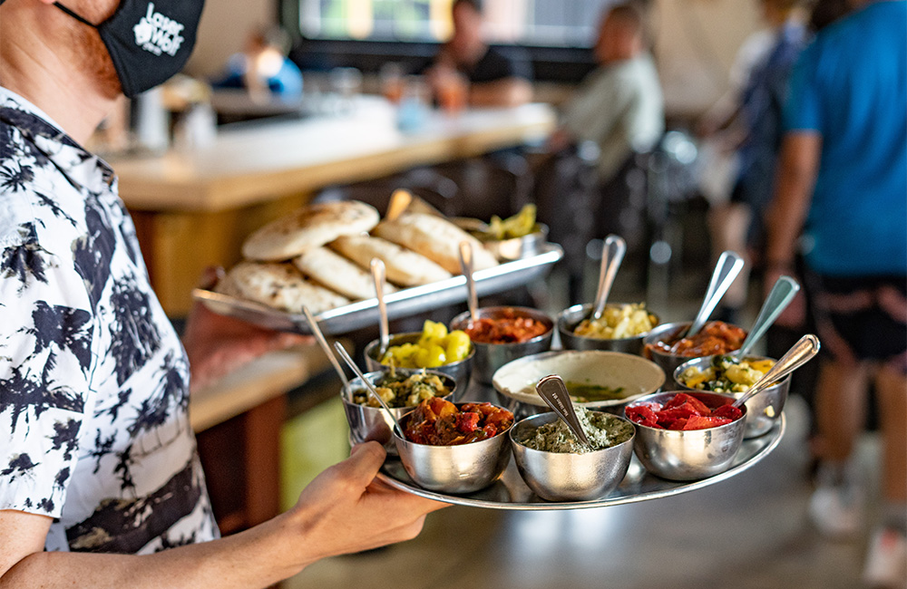 A waiter carrying two platters of meze and breads
