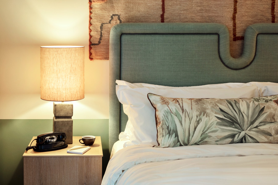 Cosy bed side lamp next to double bed with a sage green headboard and patterned cushions