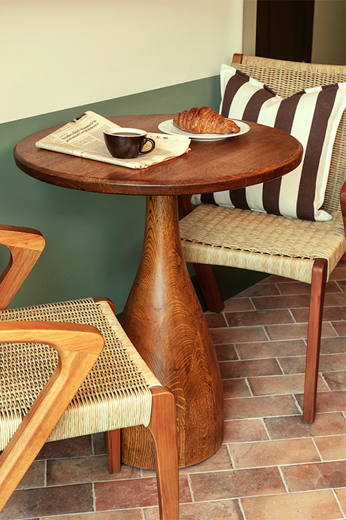 Two chairs either side of a wooden circular table with a coffee and croissant