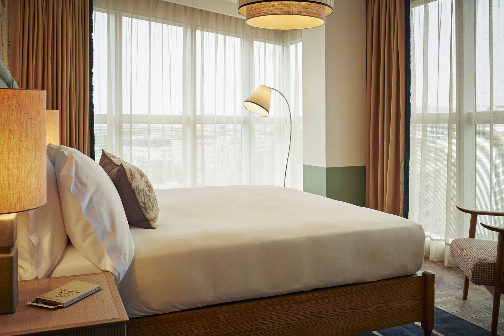 The bedroom has floor to ceiling windows on two adjacent walls, with lots of natural light