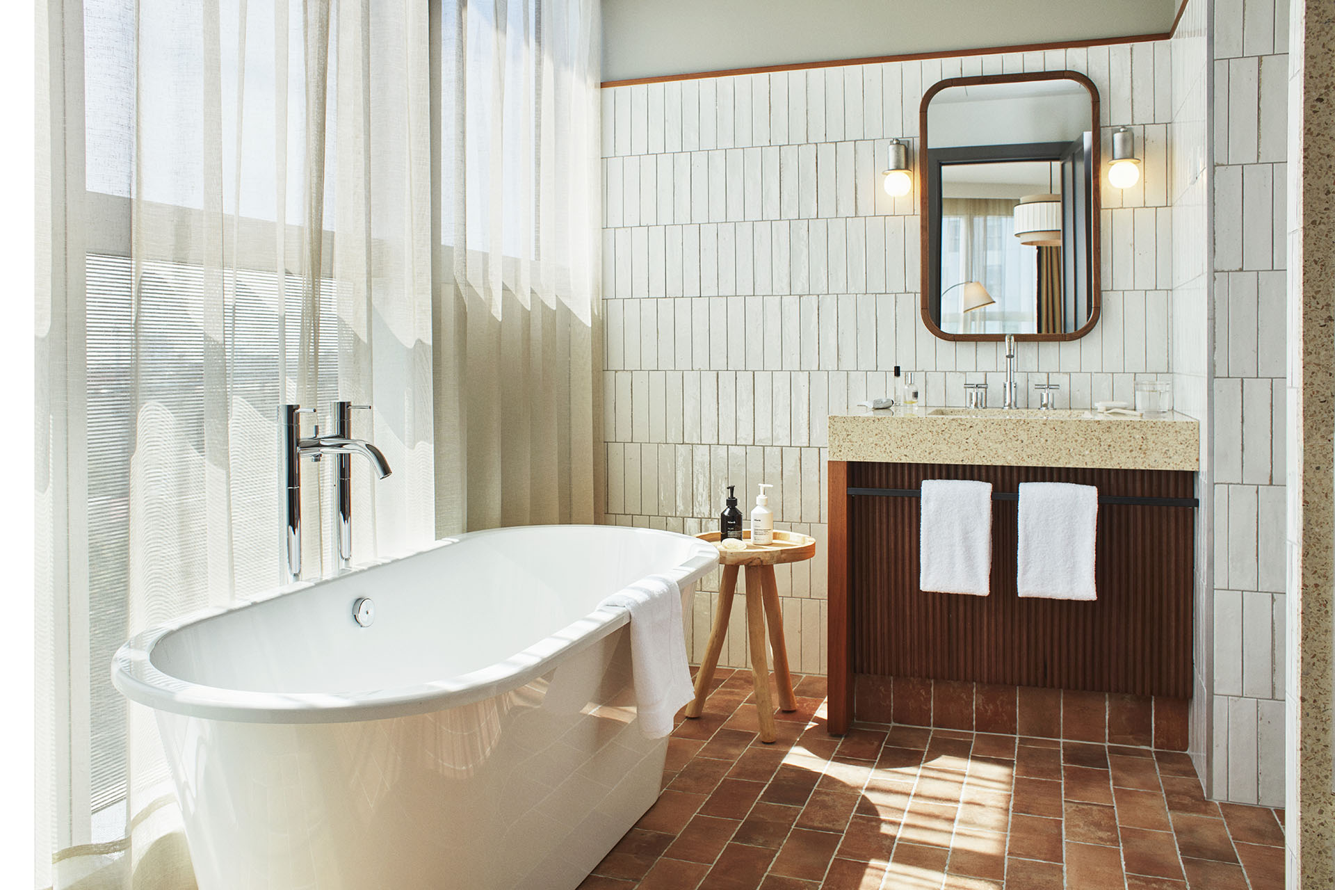 A bright and airy bathroom with standalone bath tub, and terracota tiling on the floor